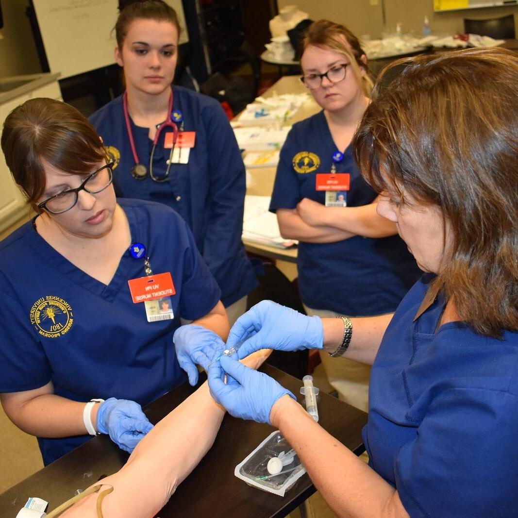 A group of nursing students using needles on a training arm